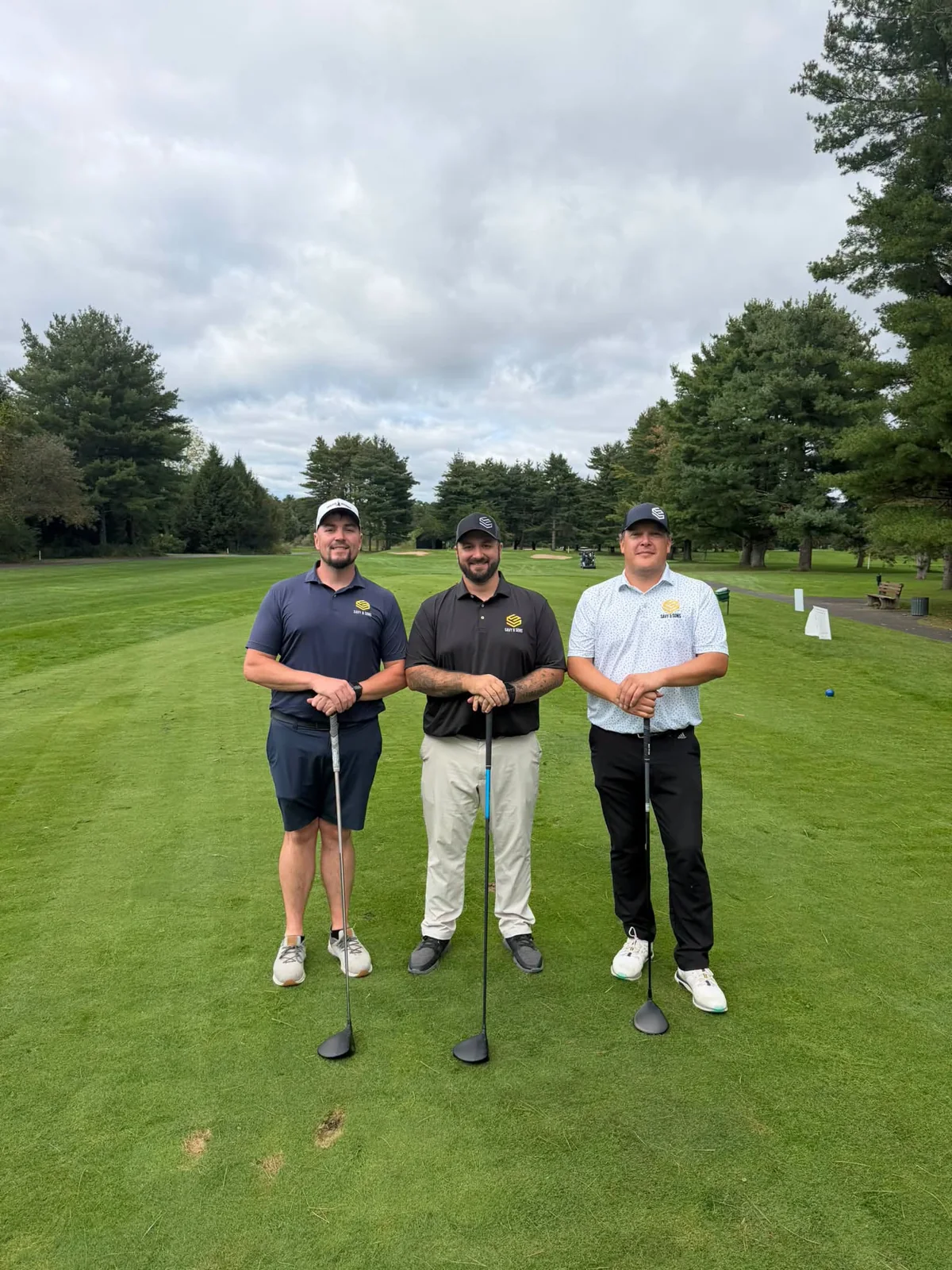 Three Savy representatives in company shirts standing with golf clubs on a golf course