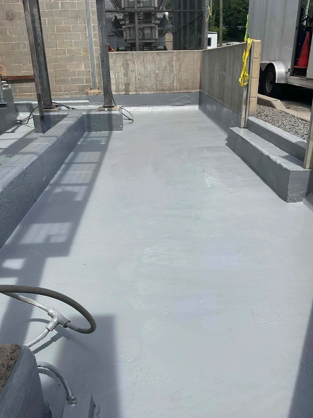 Finished gray coating across the transformer station floor and concrete curbs
